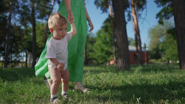 Happy family. Mother and son take their first steps. Child mother step concept. A baby is taking the first steps in the grass. Mom and baby taking first steps in the lifestyle grass.