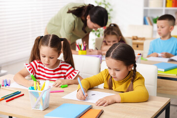 Fototapeta premium Children having lesson with teacher at wooden desks in elementary school