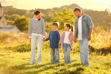 Happy family holding hands in field at sunset