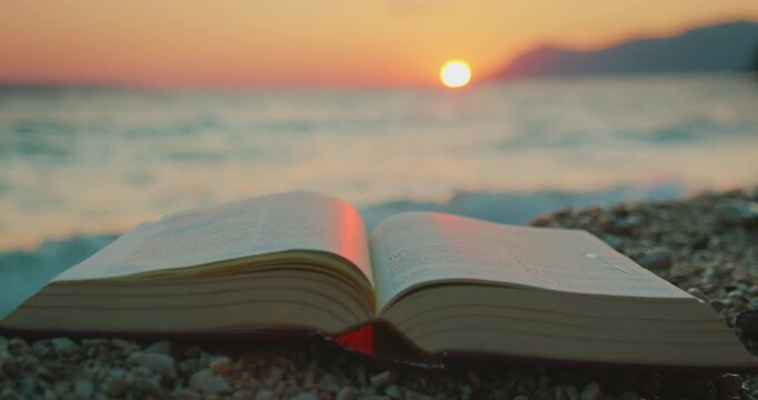 Open book lies on beach pebbles with sea waves in background at dusk