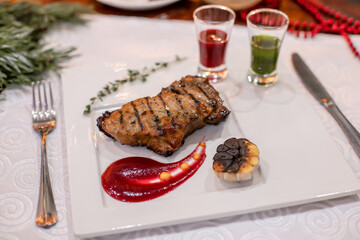 Close-up of juicy grilled meat fillet served with red puree, roasted garlic half, and fresh thyme sprig. Gourmet dish composition ideal for restaurant menu, fine dining, or festive promotion.