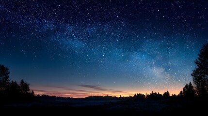 Fototapeta premium Clear, deep blue night sky transitions from dusk, showing countless stars and the faint Milky Way. Below is a dark treeline silhouette in this vast scene.