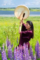 Shaman woman drumming among blooming flowers in summer