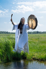 Shaman in the white dress drumming in the natural environment