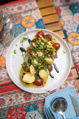 Avocado toast with cherry tomatoes mozzarella basil and balsamic on white plate