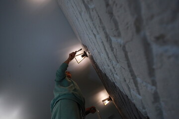 A young woman paints a brick wall with a brush in gray color