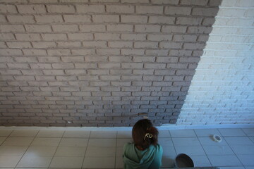 A young woman paints a brick wall with a brush in gray color