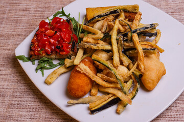 Antipasto della casa di una trattoria con verdure fritte in pastella, bruschetta con pomodori e misto fritto napoletano