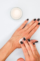 Mano mentre stende della crema per le mani sul dorso di un altra mano su uno sfondo neutro 