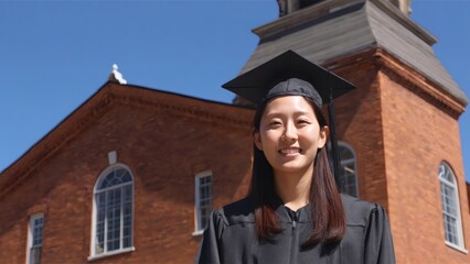 Smiling graduate in cap and gown standing in front of campus building
