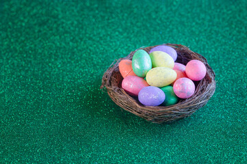 Colorful pastel Easter eggs in a rustic bird nest on a sparkling green background, with wide copy...