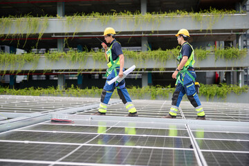 Two construction workers inspecting the solar panels installed on a rooftop, with a clear blue sky...