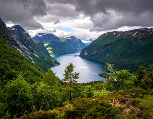 Breathtaking vista of a fjord surrounded by lush, verdant slopes under a dramatic, cloudy sky. Calm water reflecting distant mountains