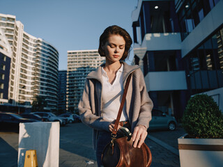 A stylish young professional woman walks through a modern urban area, adjusting her bag strap. She...