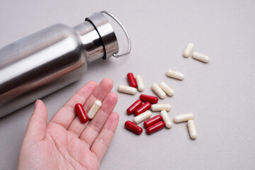 Red and white capsules next to a metal water bottle on a neutral background. Concept of sports supplements, vitamins and hydration for athletes. Modern minimalistic composition for fitness and wellnes