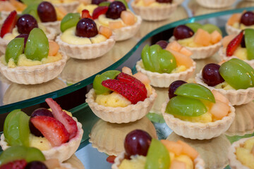 Beautiful arrangement of mini fruit tart dessert with fresh grape and strawberry topping cream filling in shortcrust pastry. sweet food perfect for party or buffet
