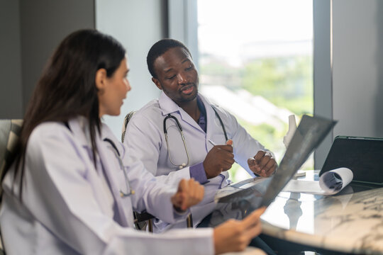 Diverse medical team african male doctor and female doctor collaborating and reviewing medical documents writing and discussing patient data in hospital office, teamwork in healthcare, patient care - Powered by Adobe