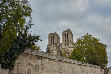 Gothic towers of Notre Dame Cathedral in Paris with a gray sky and trees in the foreground in a historic setting