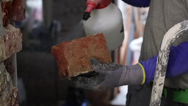 A young man wets one brick with a spray bottle.