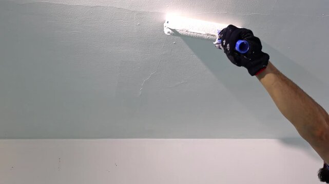 A man is painting the ceiling in the living room with a roller.