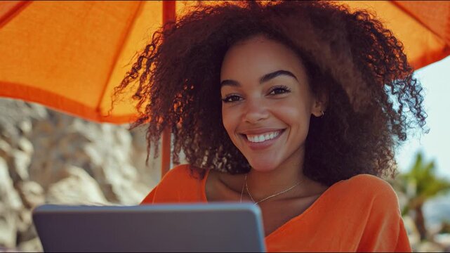 Smiling young woman lying on sunbed on the beach reading a book on tablet under the parasol