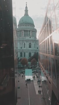 Majestic Saint Paul's Cathedral viewed from between modern glass buildings, with people walking below and the warm light of the golden hour reflecting on the windows of the financial district