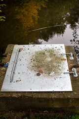 Obraz premium Metal cover rests on a stone platform near a calm water surface surrounded 