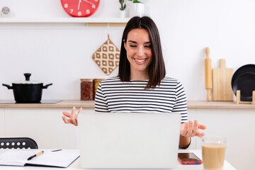 Smiling female freelancer working remotely from home, having a video call on her laptop in her...