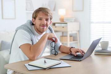 Man with glasses using laptop at wooden table indoors