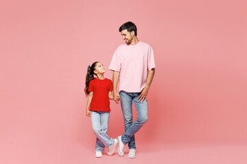 Fototapeta premium Full body young smiling happy parent man with child girl wear red casual clothes. Daddy little kid daughter standing holding hands isolated on plain pink background. Father's Day Love family concept.