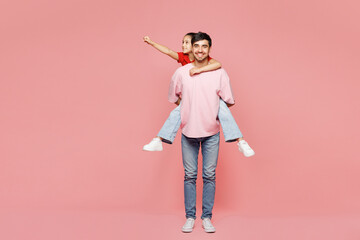 Full body young parent man with child girl wearing red casual clothes. Daddy little kid daughter give piggyback ride to joyful, sit on back isolated on plain pink background Father's Day Love concept