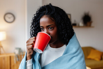 Young adult Latin American woman holding hot coffee cup while looking through the window at home....
