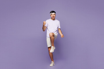 Full body young strong fitness trainer instructor man sportsman he wear sportswear train in home gym do winner gesture raise up leg isolated on plain purple background. Workout sport fit abs concept.