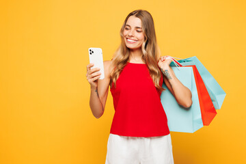 Young woman wear red casual clothes hold in hand paper package bags after shopping use mobile cell...