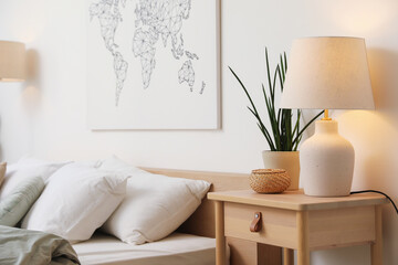 Bed with linens, nightstand, houseplant and lamp near white wall in bedroom