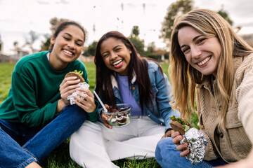 Diverse group of young women laughing and sharing lunch on a sunny park picnic, enjoying...