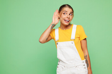 Young curious nosy happy woman wear yellow t-shirt overall casual clothes try to hear you overhear listening intently isolated on plain pastel light green background studio portrait Lifestyle concept.
