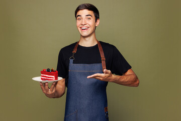 Young man barista bartender barman employee wear jeans apron black t-shirt work in coffee shop bring point hand on cake dessert order isolated on plain green background Small business startup concept