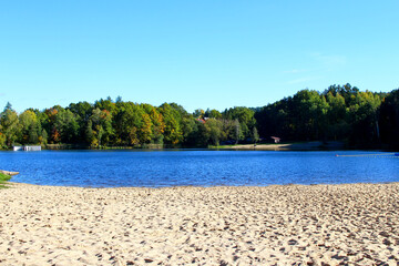 Scenic lakeside view with sandy beach and vibrant autumn foliage at midday