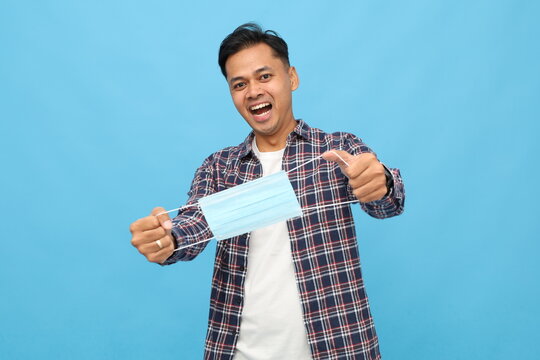 Young asian man shouting in casual clothes posing isolated on blue background, fast spreading epidemic pandemic, coronavirus 2019-NCOV, SARS, COVID-19, flu virus concept, holding sterile face mask. - Powered by Adobe
