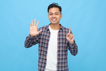 Young Asian man wearing casual clothes, counting or showing number six with fingers, standing...