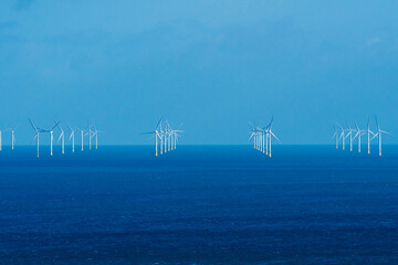 Rows of offshore wind turbines rising from deep blue water © Philip