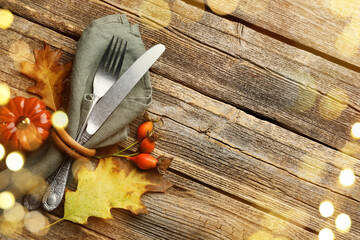 Autumn place setting, bokeh lights. Cutlery, napkin and fall decor on wooden table, top view