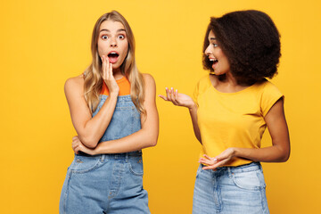 Side profile view two shocked surprised young friends buddies women they wearing denim casual clothes talk speak together isolated on plain yellow orange background studio portrait. Lifestyle concept.