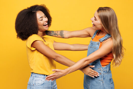 Side profile view two young friends buddies women wear denim casual clothes going to hug each other together greet meet isolated on plain yellow orange background studio portrait. Lifestyle concept.
