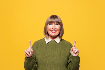 Elderly smiling happy blonde woman she wear green sweater casual clothes point index finger...