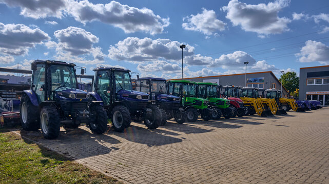 Row of new Farmtrac and Deutz-Fahr tractors in multiple colors on importer yard in Winsen, Germany, showing modern compact agricultural machines ready for sale