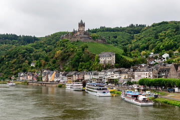 Cochem, Germany - September 9, 2025: Reichsburg Cochem Castle overlooking the Moselle River and old town of Cochem, Germany, with cruise boats on the autumn waterfront.