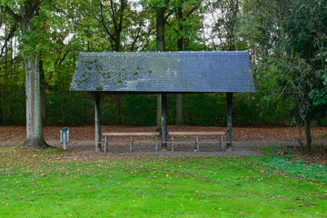 Covered benches in the forest, for picnicking with green grass in the foreground. Belgium