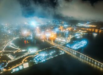 Aerial view of the brightly illuminated casino and hotel district of Macau glowing through a misty and foggy night.
